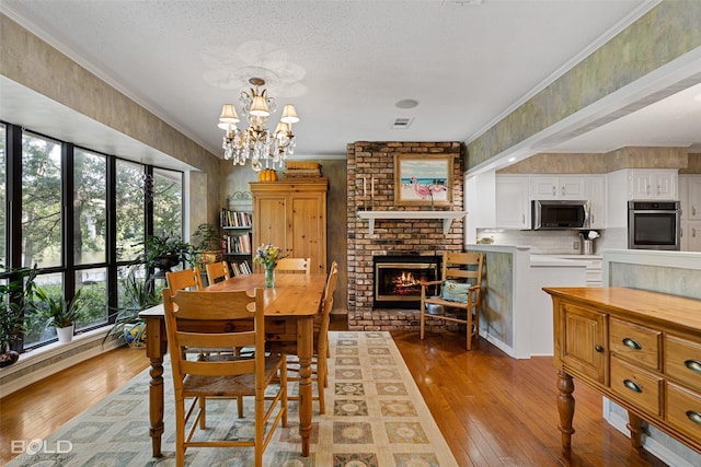 dining room featuring crown molding, a brick fireplace, a notable chandelier, and light hardwood / wood-style flooring