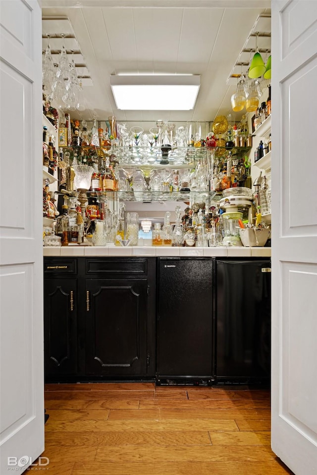 bar featuring light wood-type flooring and black refrigerator