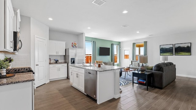 kitchen with light stone countertops, a center island with sink, white cabinets, and appliances with stainless steel finishes