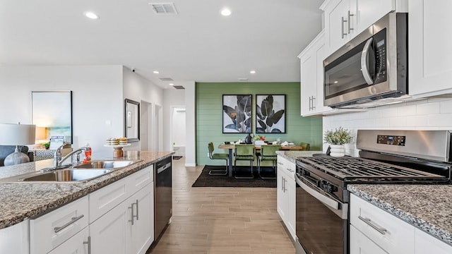 kitchen featuring white cabinets, appliances with stainless steel finishes, light stone counters, and sink