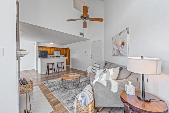 living room featuring ceiling fan, light hardwood / wood-style flooring, and a towering ceiling