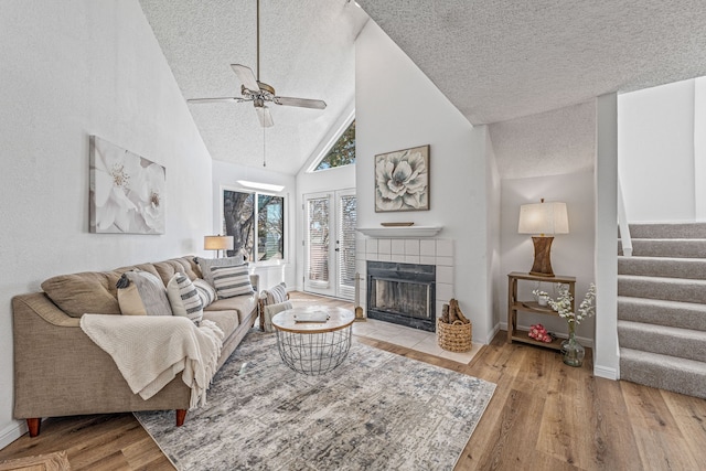 living room featuring ceiling fan, stairs, a fireplace, wood finished floors, and a textured ceiling