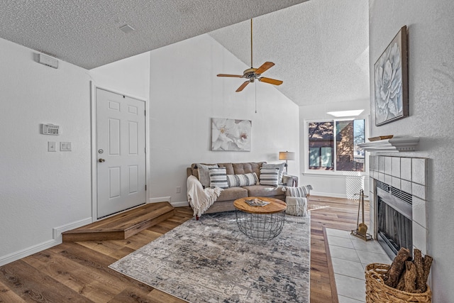 living room with ceiling fan, a tile fireplace, light hardwood / wood-style floors, and a textured ceiling