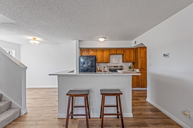 kitchen with light wood finished floors, stainless steel electric range, brown cabinets, and freestanding refrigerator