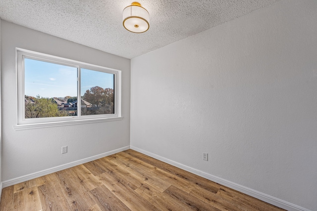 empty room featuring a textured wall, a textured ceiling, baseboards, and wood finished floors