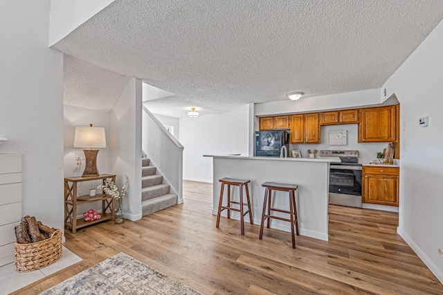 kitchen featuring black refrigerator, a kitchen breakfast bar, light hardwood / wood-style floors, a textured ceiling, and electric stove