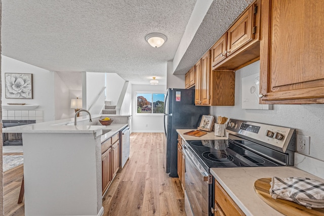 kitchen featuring sink, a breakfast bar, appliances with stainless steel finishes, light hardwood / wood-style floors, and a textured ceiling