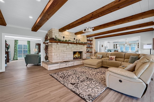 living room with beamed ceiling, a stone fireplace, and light hardwood / wood-style floors