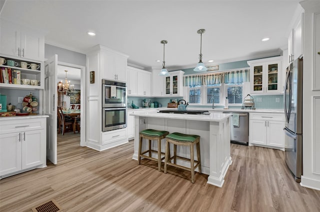 kitchen with a kitchen island, pendant lighting, white cabinetry, stainless steel appliances, and light hardwood / wood-style flooring