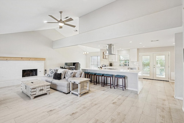 living room with ceiling fan with notable chandelier, light hardwood / wood-style floors, and vaulted ceiling