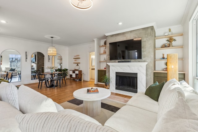 living room with built in shelves, crown molding, a high end fireplace, and light hardwood / wood-style flooring