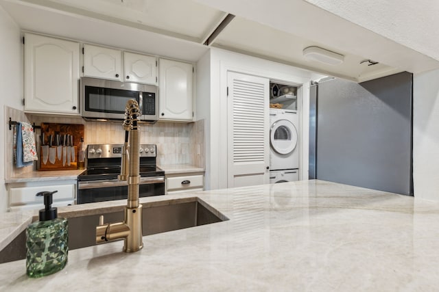 kitchen with stacked washing maching and dryer, backsplash, stainless steel appliances, and white cabinetry