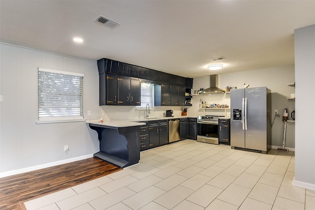 kitchen with kitchen peninsula, wall chimney exhaust hood, a breakfast bar, stainless steel appliances, and sink