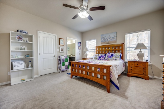 bedroom featuring ceiling fan, multiple windows, light colored carpet, and ensuite bath