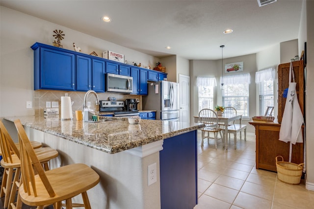 kitchen with appliances with stainless steel finishes, decorative backsplash, hanging light fixtures, kitchen peninsula, and blue cabinetry