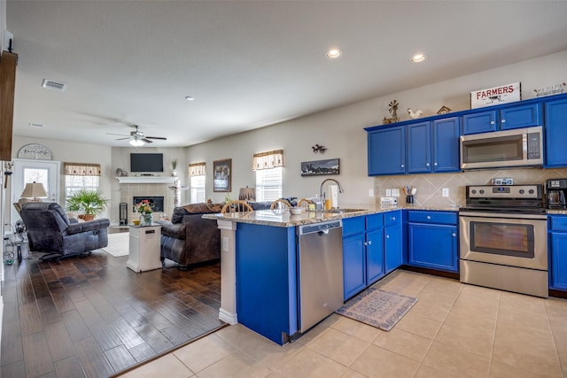 kitchen with appliances with stainless steel finishes, blue cabinets, light stone counters, a tile fireplace, and sink