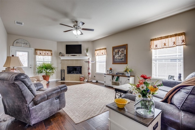 living room featuring ceiling fan, a tiled fireplace, dark hardwood / wood-style flooring, and a wealth of natural light