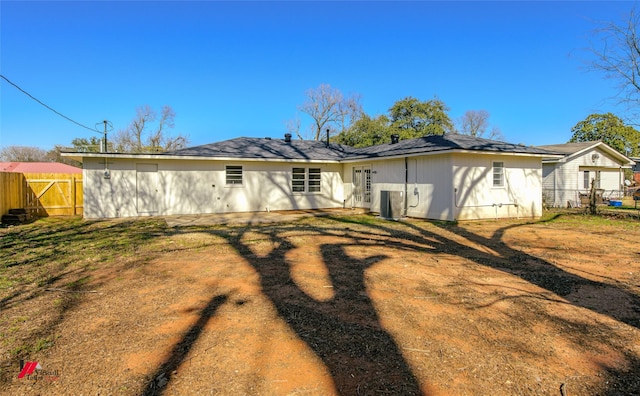 rear view of house with central AC unit and a lawn