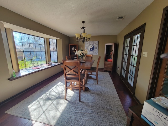 dining room with french doors, a textured ceiling, dark hardwood / wood-style floors, and an inviting chandelier