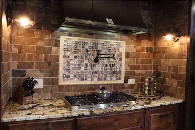 bar featuring light stone counters, dark brown cabinets, stainless steel gas stovetop, and decorative backsplash