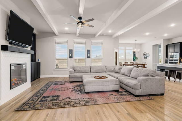 living area featuring light wood-style flooring, a glass covered fireplace, beam ceiling, and baseboards