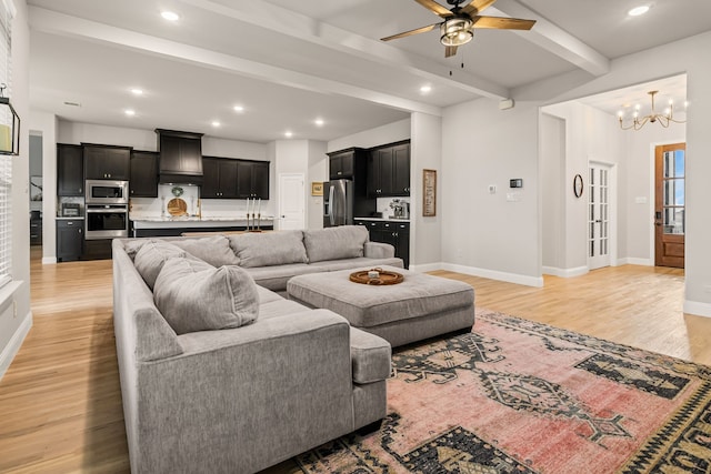 living room with ceiling fan with notable chandelier, light hardwood / wood-style floors, and beamed ceiling