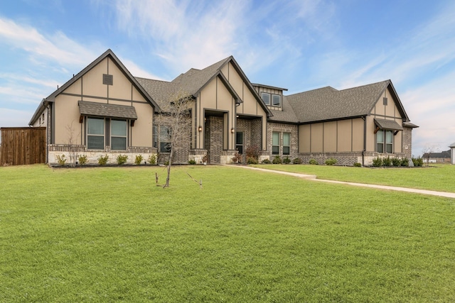 tudor home featuring brick siding, a shingled roof, fence, and a front yard