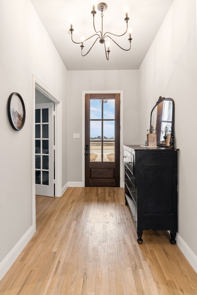 doorway with baseboards, light wood-style flooring, and an inviting chandelier