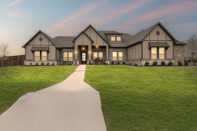 tudor home featuring a shingled roof, fence, a yard, stone siding, and board and batten siding