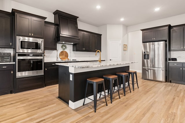 kitchen featuring light wood-style flooring, decorative backsplash, appliances with stainless steel finishes, a sink, and a kitchen bar