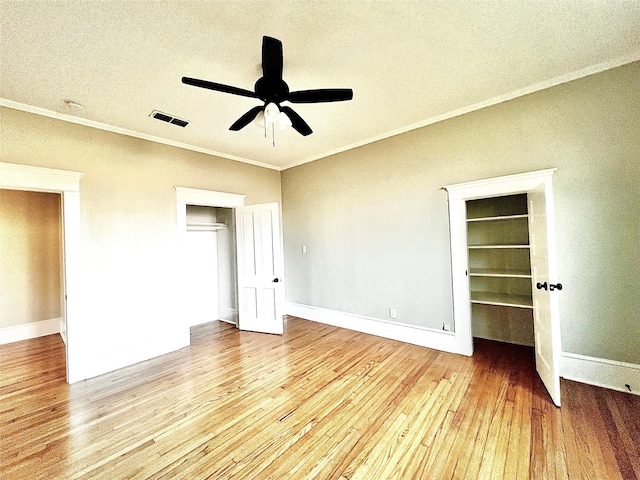 unfurnished bedroom with a walk in closet, ornamental molding, a closet, ceiling fan, and light hardwood / wood-style floors