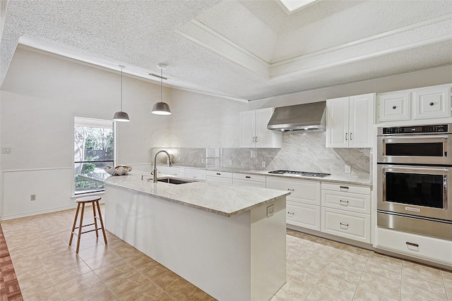 kitchen with sink, wall chimney exhaust hood, light stone countertops, decorative light fixtures, and white cabinetry