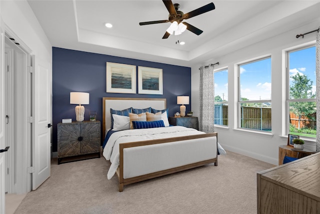 carpeted bedroom with a raised ceiling and ceiling fan