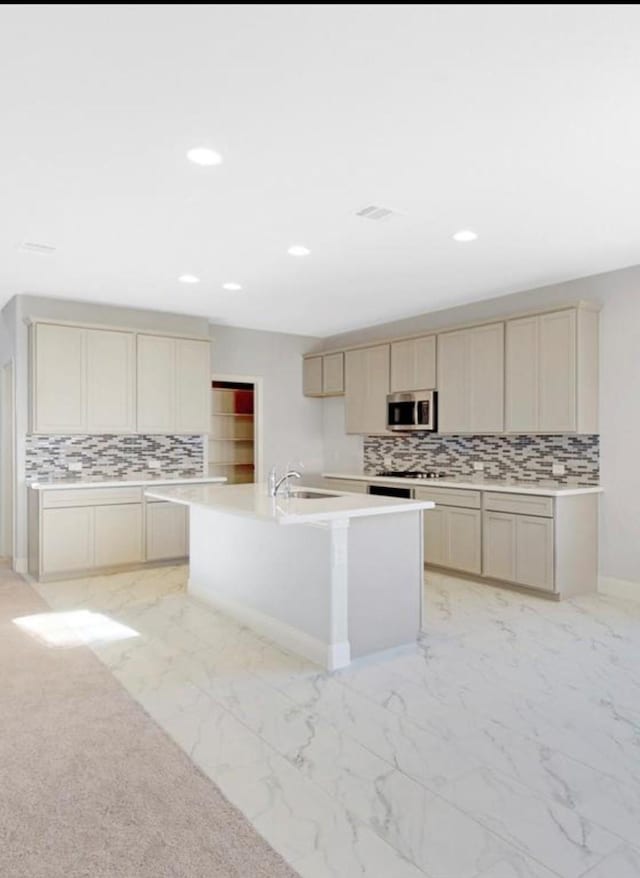 kitchen with a center island with sink, backsplash, and cream cabinets