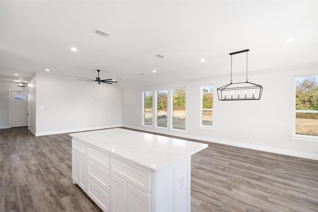 kitchen with light stone counters, decorative light fixtures, a center island, hardwood / wood-style floors, and white cabinets