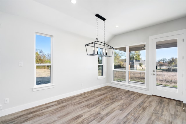 unfurnished dining area with wood-type flooring, vaulted ceiling, and a notable chandelier