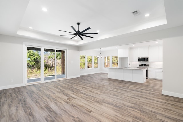 unfurnished living room with a raised ceiling, sink, and light hardwood / wood-style floors