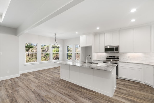 kitchen with hanging light fixtures, stainless steel appliances, light stone counters, an island with sink, and white cabinets