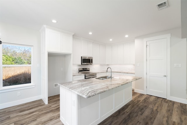 kitchen with sink, light stone counters, an island with sink, stainless steel appliances, and white cabinets