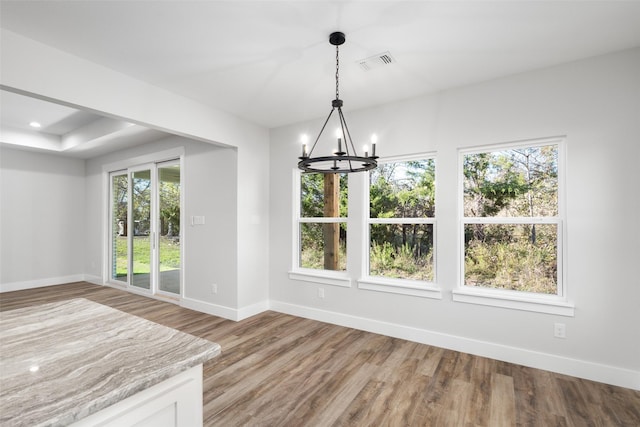 unfurnished dining area with wood-type flooring, plenty of natural light, and an inviting chandelier