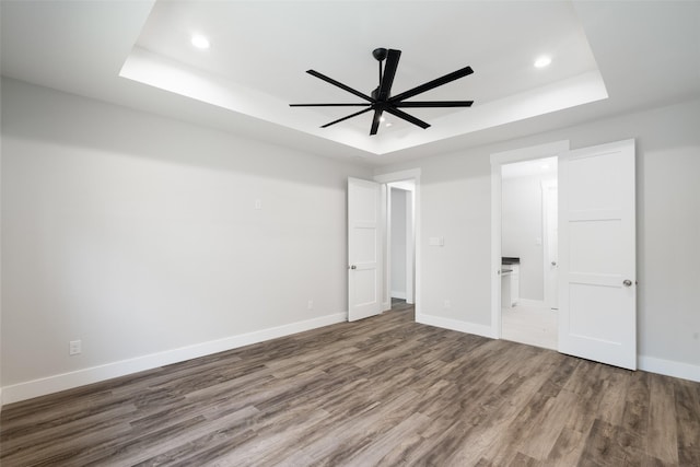 unfurnished bedroom featuring hardwood / wood-style flooring, ensuite bath, a raised ceiling, and ceiling fan