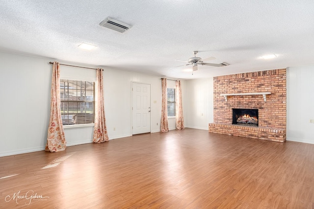 unfurnished living room with a fireplace, ceiling fan, a textured ceiling, and dark wood-type flooring