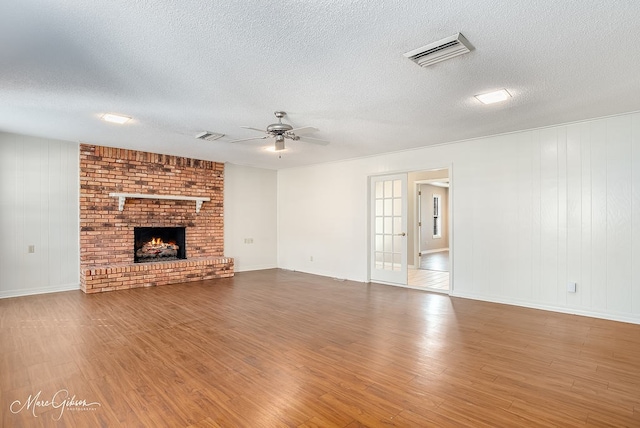 unfurnished living room with a fireplace, wood-type flooring, a textured ceiling, and ceiling fan