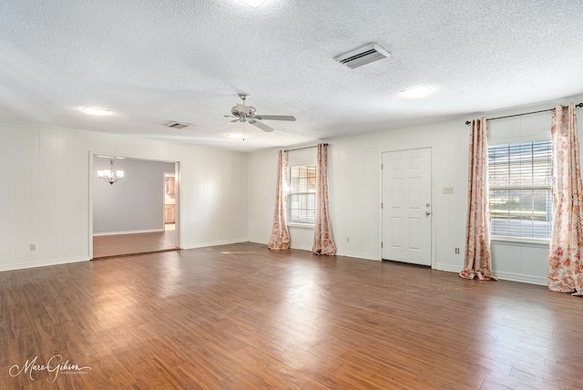 spare room featuring a textured ceiling, ceiling fan with notable chandelier, a wealth of natural light, and dark wood-type flooring