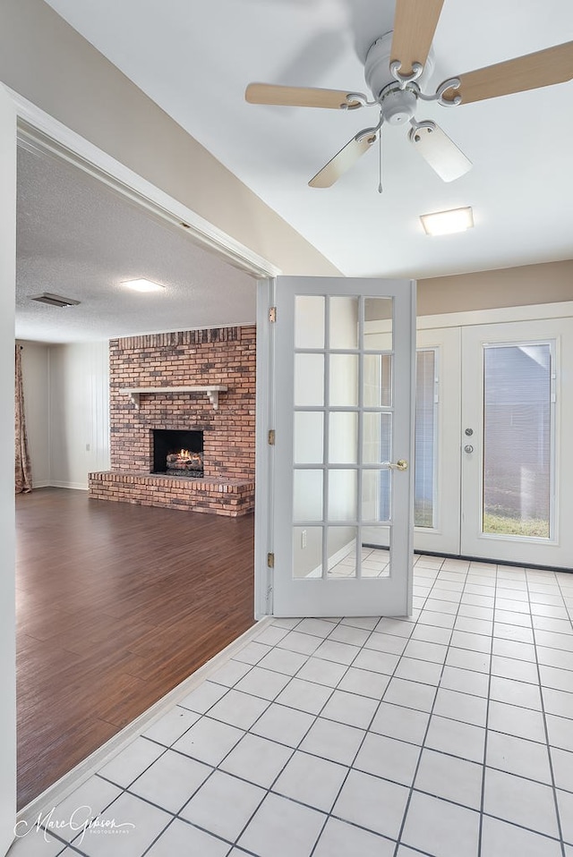 unfurnished living room featuring ceiling fan, light tile patterned floors, a fireplace, and french doors