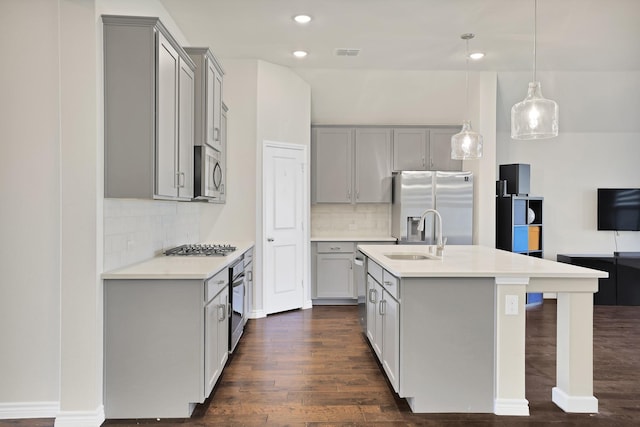 kitchen with sink, hanging light fixtures, stainless steel appliances, tasteful backsplash, and a center island with sink