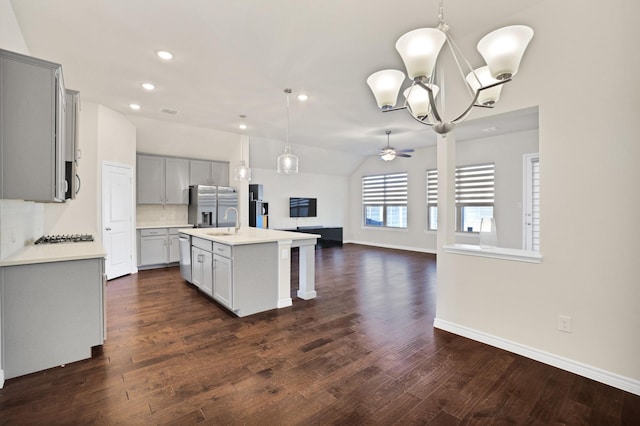 kitchen featuring appliances with stainless steel finishes, tasteful backsplash, ceiling fan with notable chandelier, vaulted ceiling, and a kitchen island with sink