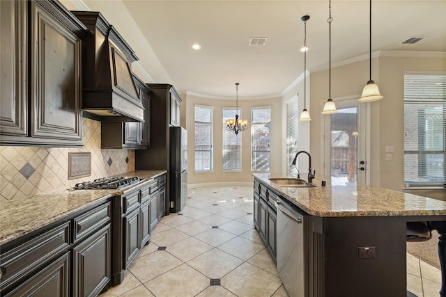 kitchen featuring sink, an island with sink, appliances with stainless steel finishes, decorative light fixtures, and a chandelier