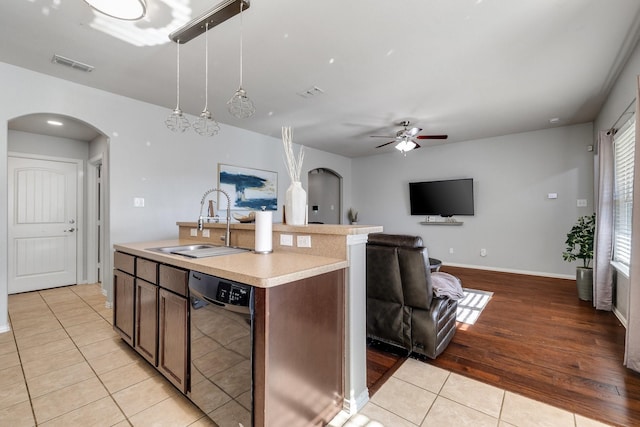 kitchen with light tile patterned flooring, pendant lighting, sink, black dishwasher, and a kitchen island with sink