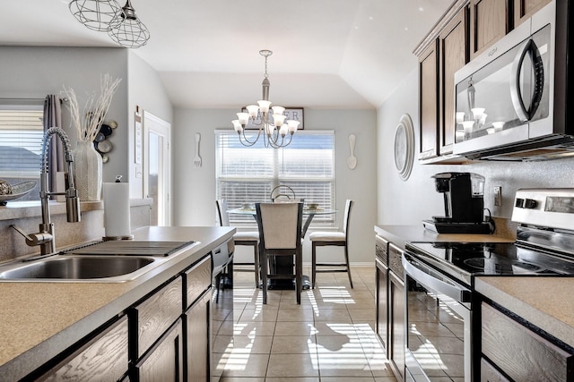 kitchen featuring stainless steel appliances, vaulted ceiling, sink, a notable chandelier, and hanging light fixtures